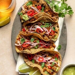 four tempeh tacos on a large platter with lime wedges and cilantro.