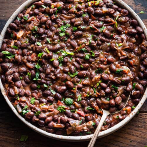 Overhead view of shallow tan bowl filled with black beans on a wooden table.