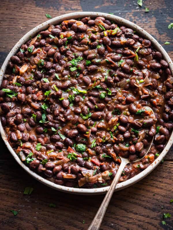 Overhead view of shallow tan bowl filled with black beans on a wooden table.