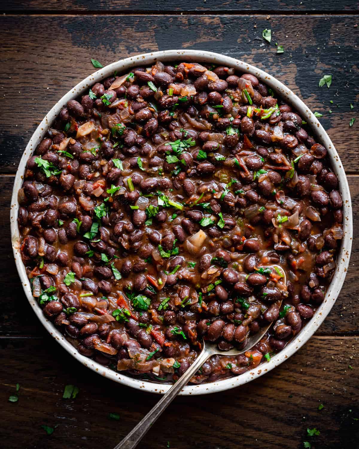 Overhead view of shallow tan bowl filled with black beans on a wooden table.