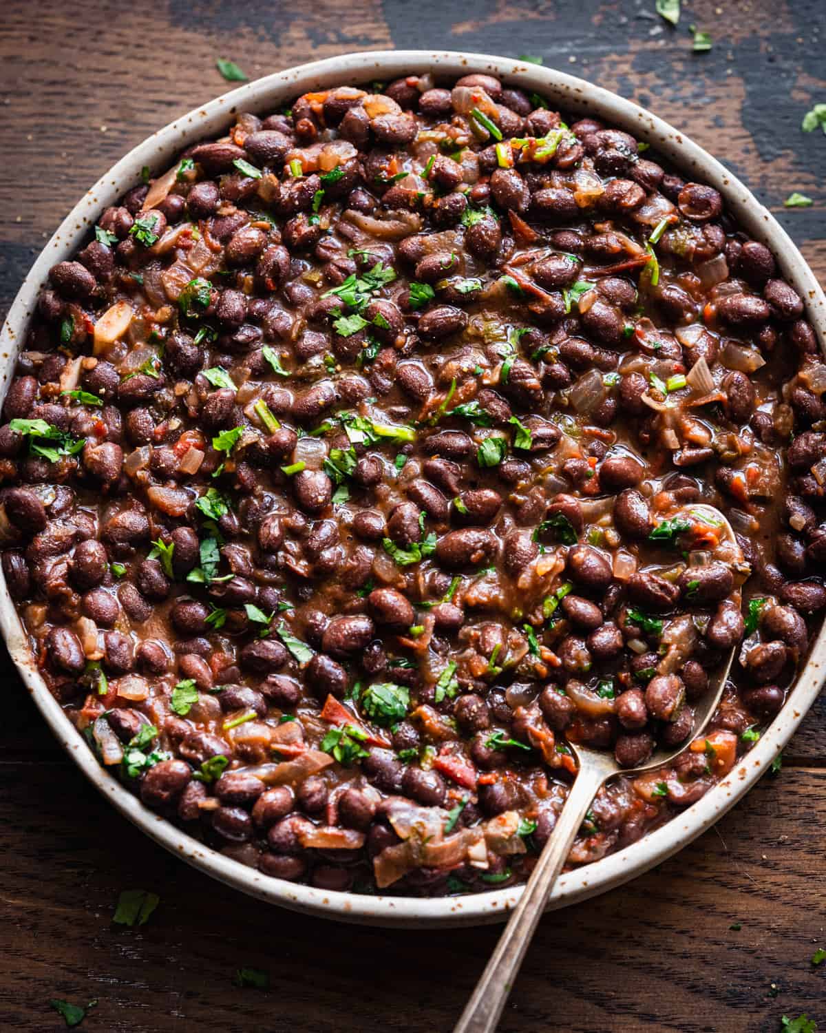 Overhead close up of shallow tan bowl filled with black beans on a wooden table.