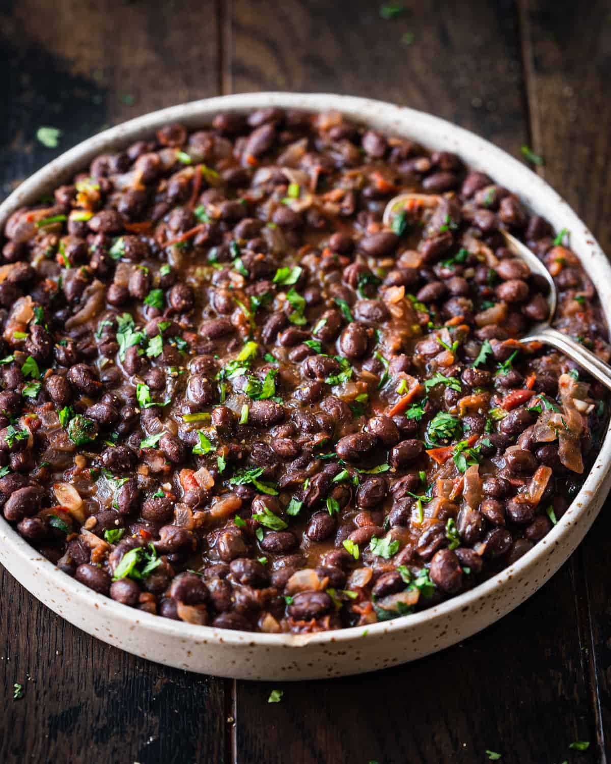 Side view of shallow tan bowl filled with black beans on a wooden table.