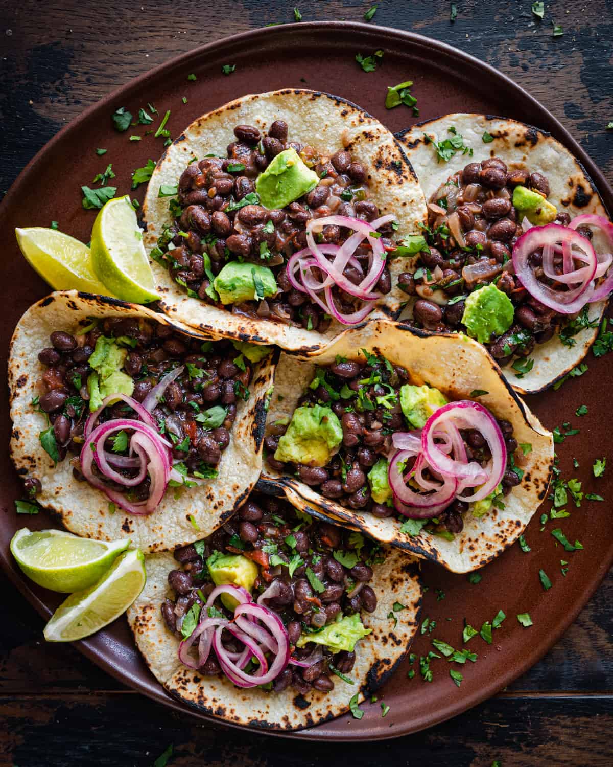 Overhead view of black bean tacos and lime wedges on brown plate.