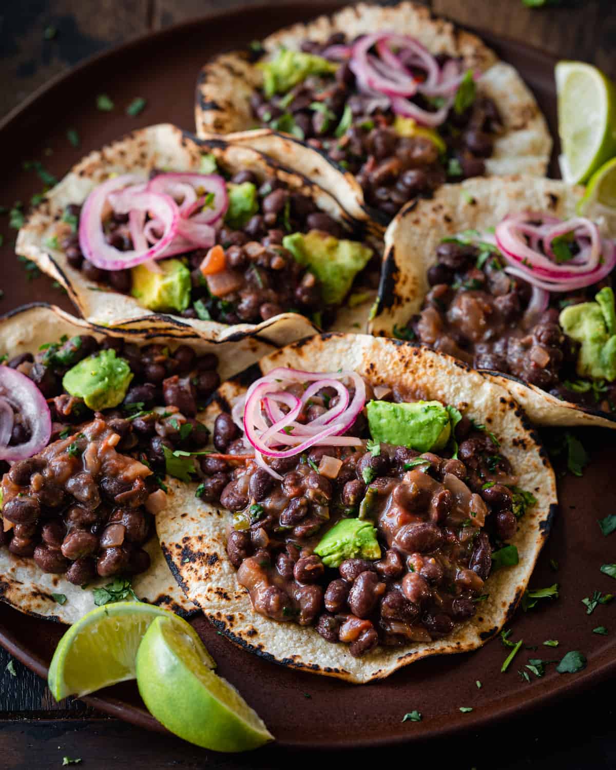 Side view of black bean tacos and lime wedges on brown plate.