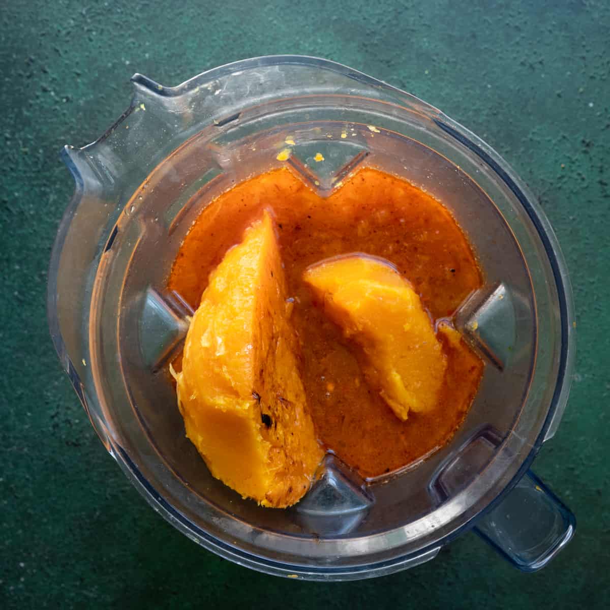 roasted butternut squash halves added to a blender with broth on a green surface. 