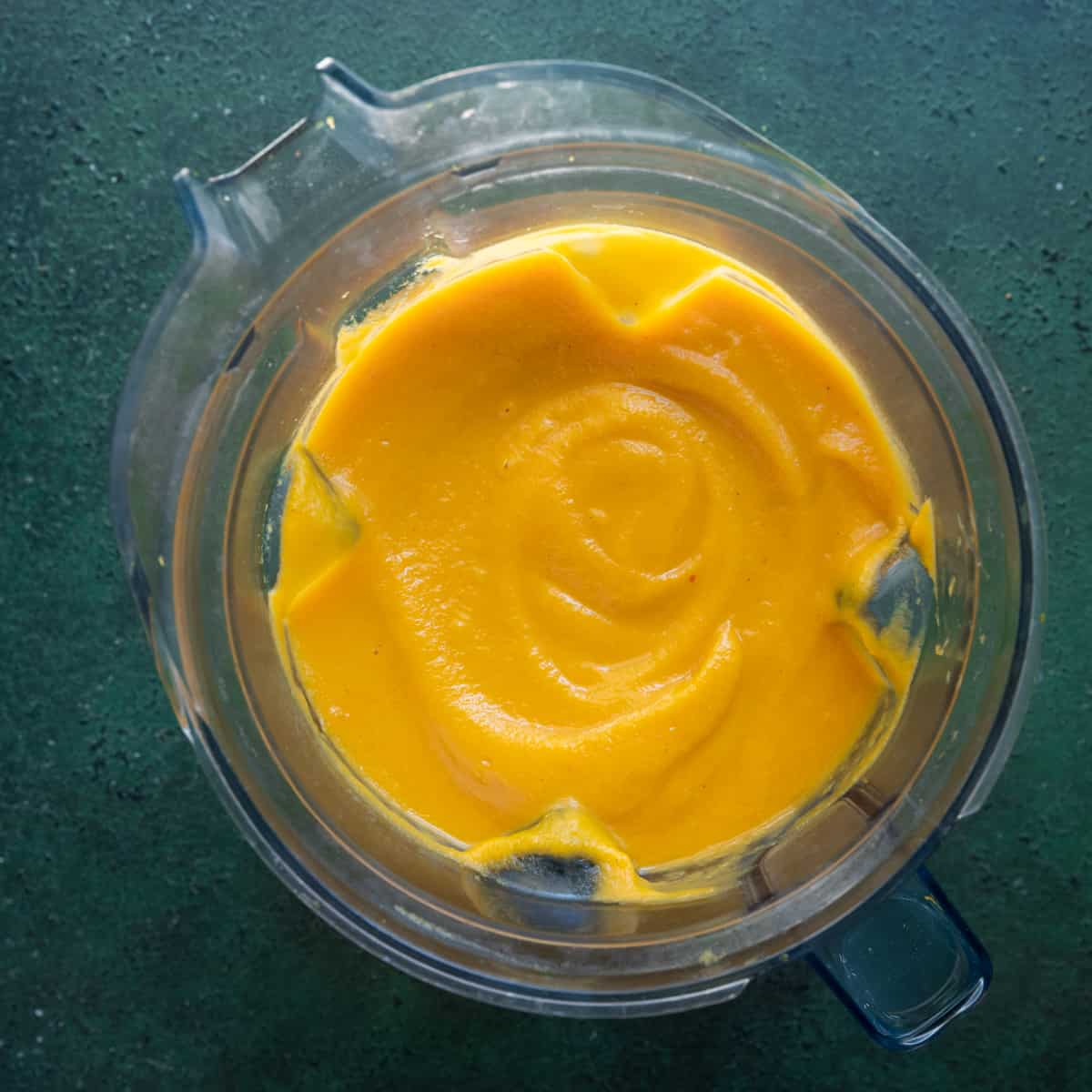 creamy pureed butternut squash soup in a blender on a green surface. 