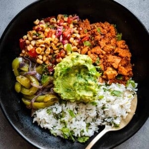 Burrito bowl components together in black bowl with a spoon.