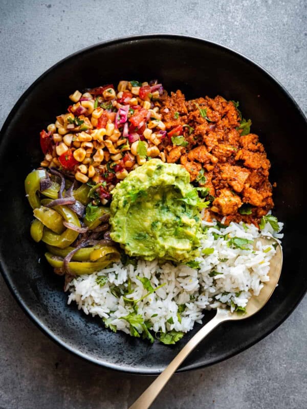 Burrito bowl components together in black bowl with a spoon.