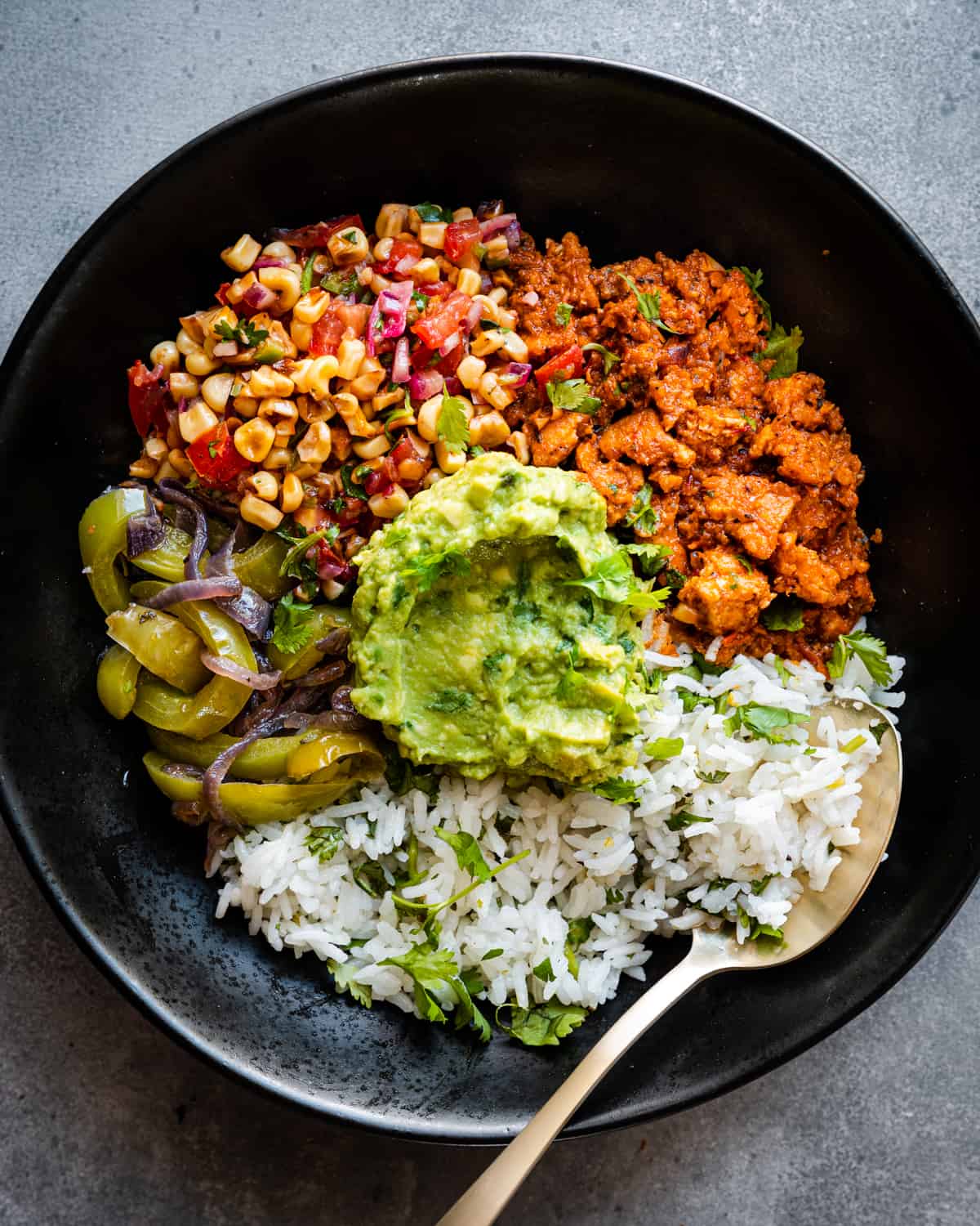 Burrito bowl components together in black bowl with a spoon.