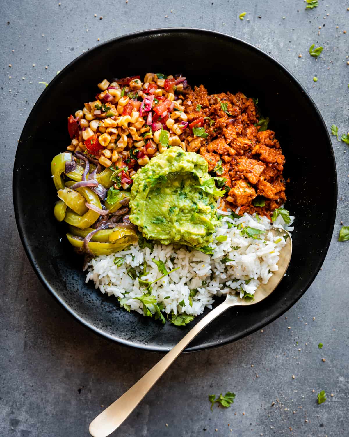 Burrito bowl components together in black bowl with a spoon.