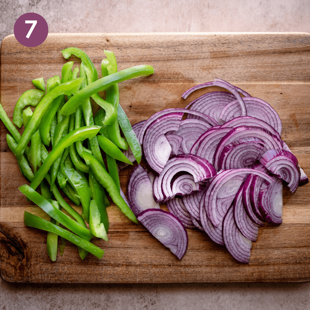 Thinly sliced green bell pepper and red onion on a wooden cutting board.