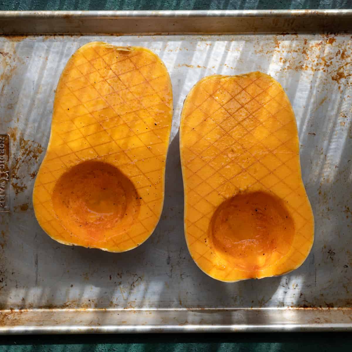 two large crosshatched butternut squash halves on a sheet pan, rubbed with olive oil.