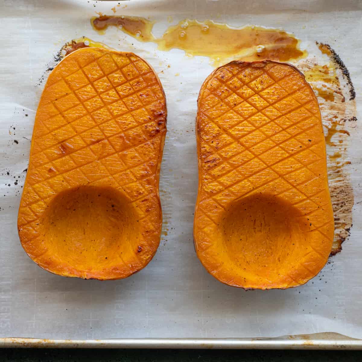 two roasted butternut squash halves on a sheet pan with crosshatch marks. 