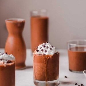 Four glasses of chocolate sweet potato milkshake, two with whipped cream, on a pink table.