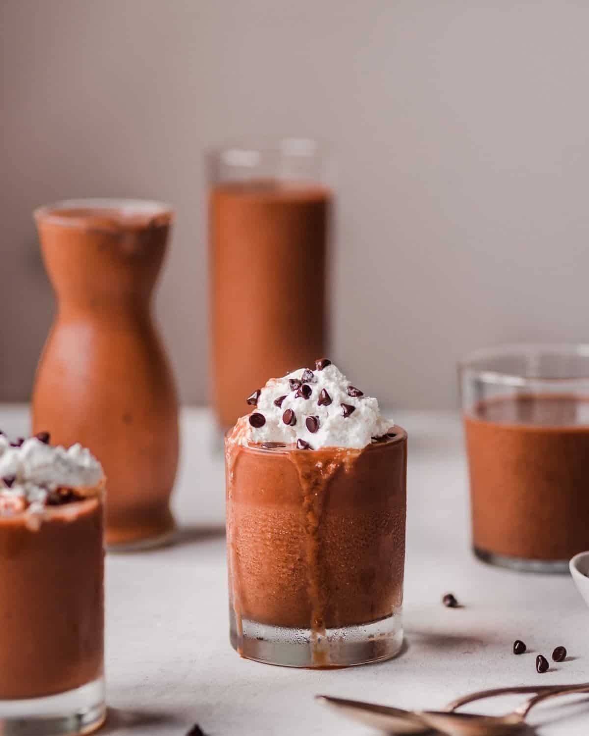 Four glasses of chocolate sweet potato milkshake, two with whipped cream, on a pink table.