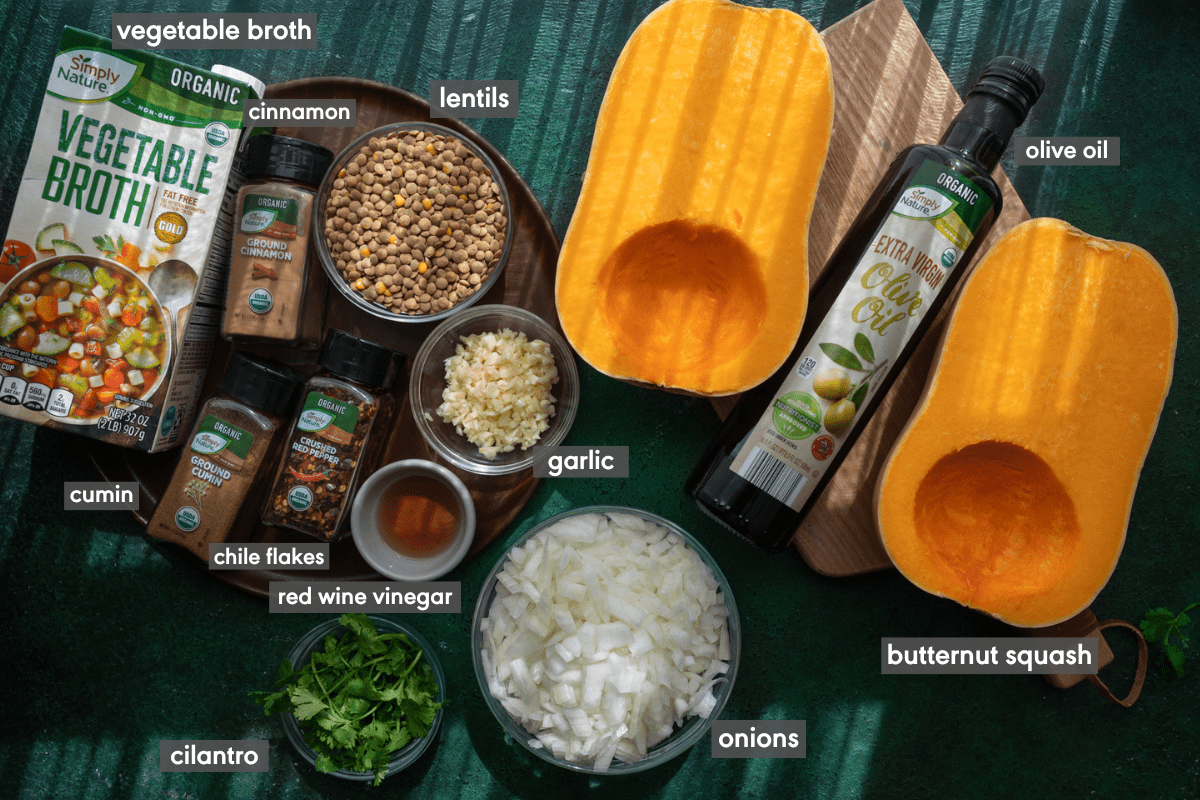 ingredients for butternut squash soup with lentils laid on green surface with ingredients labeled.