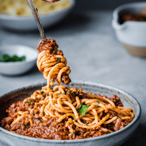 person twirling bolognese around a fork in a bowl.