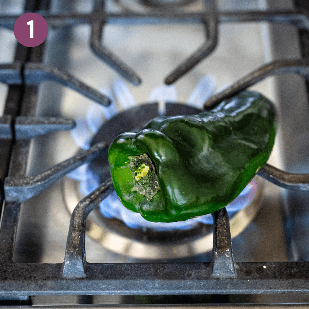 Poblano pepper roasting on an open flame on the stovetop.