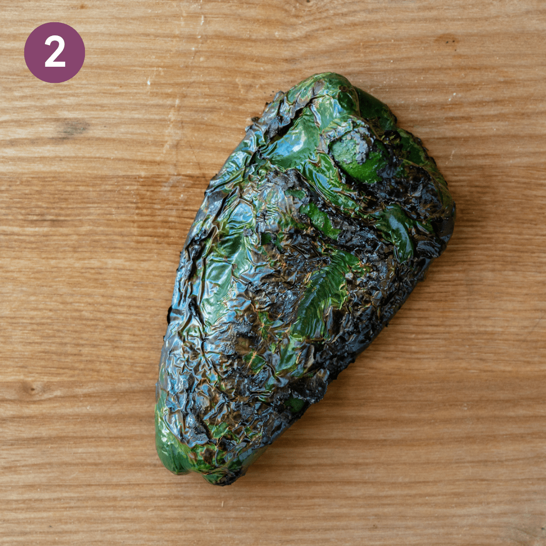 Broiled poblano pepper on a wooden cutting board.