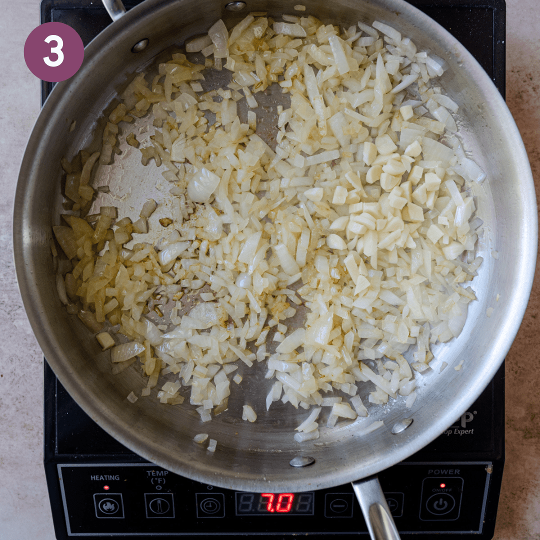 Onions and garlic being sauteed in a deep sauté pan.