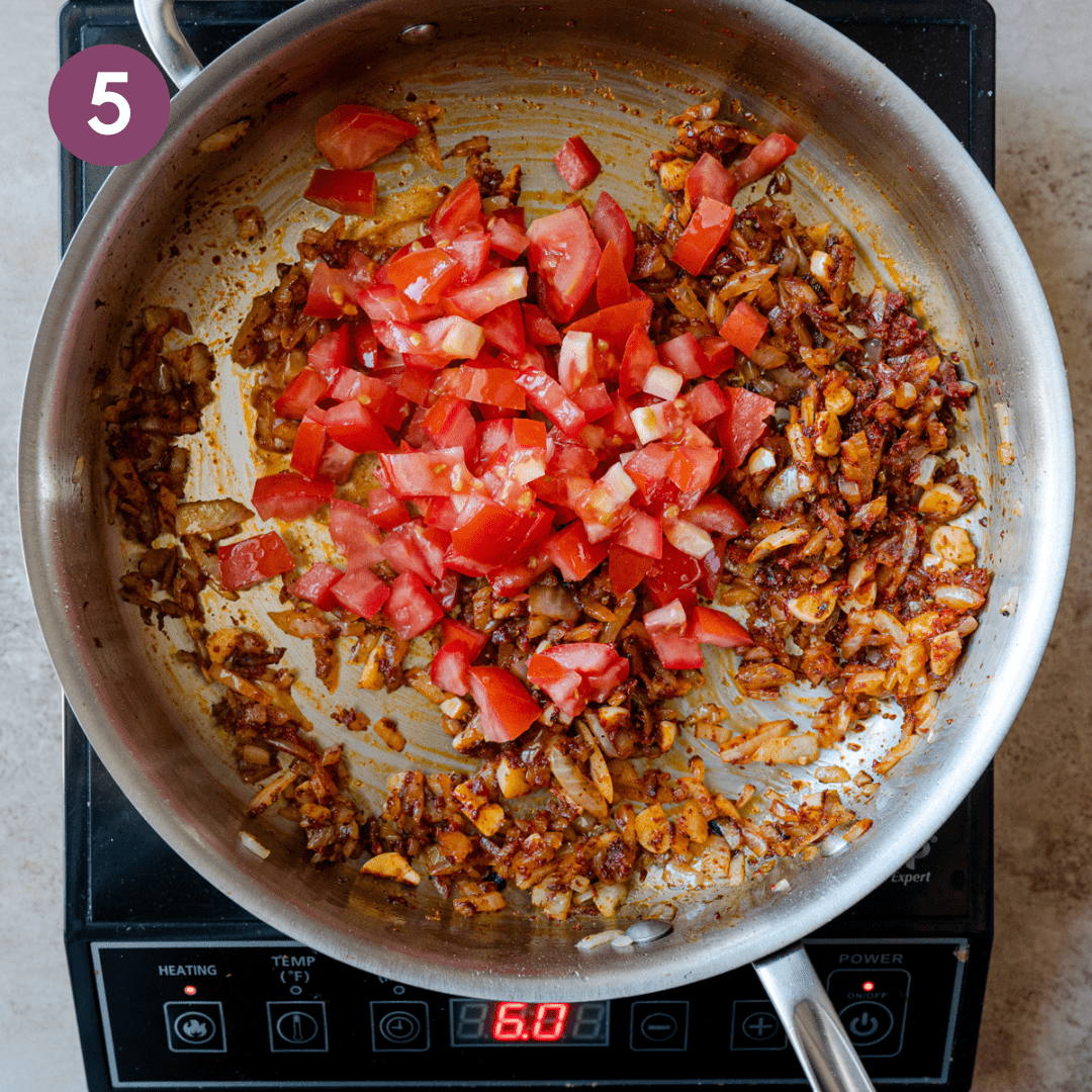 Chopped tomatoes on top of sauteed onion and spice mixture in a frying pan. 