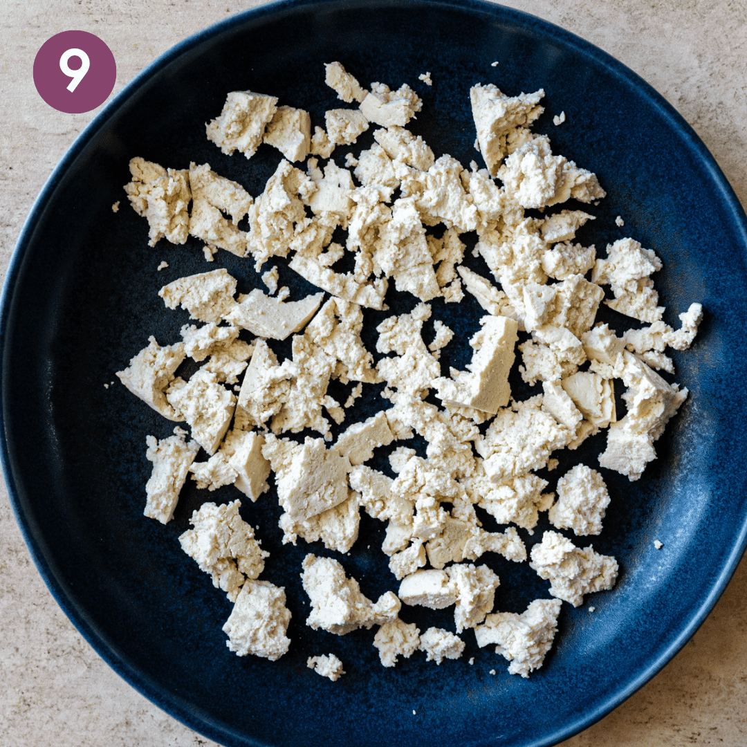 Crumbled tofu on navy blue plate on a light colored table.