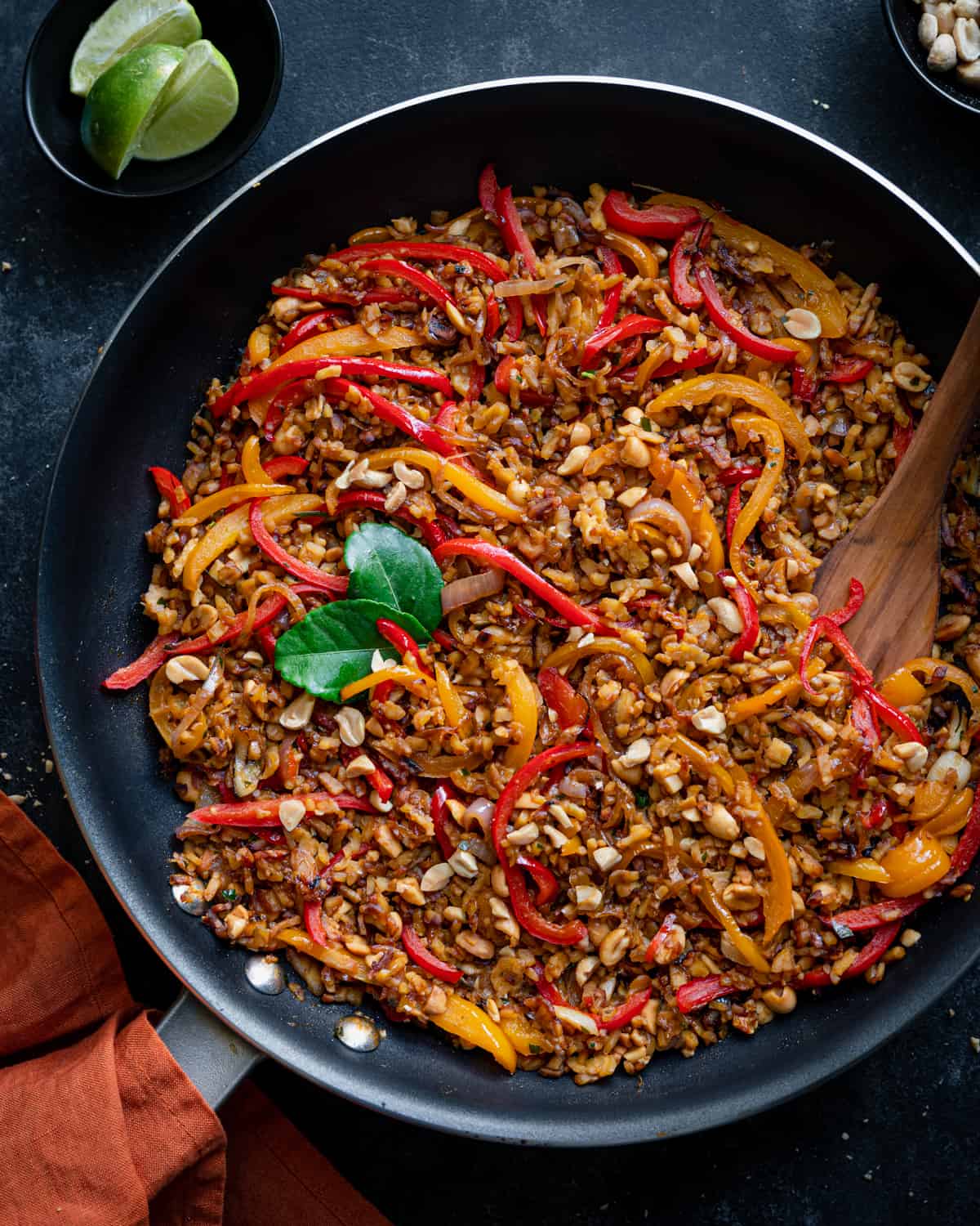 indonesian tempeh stir fry with bell peppers in a black skillet on a black board.