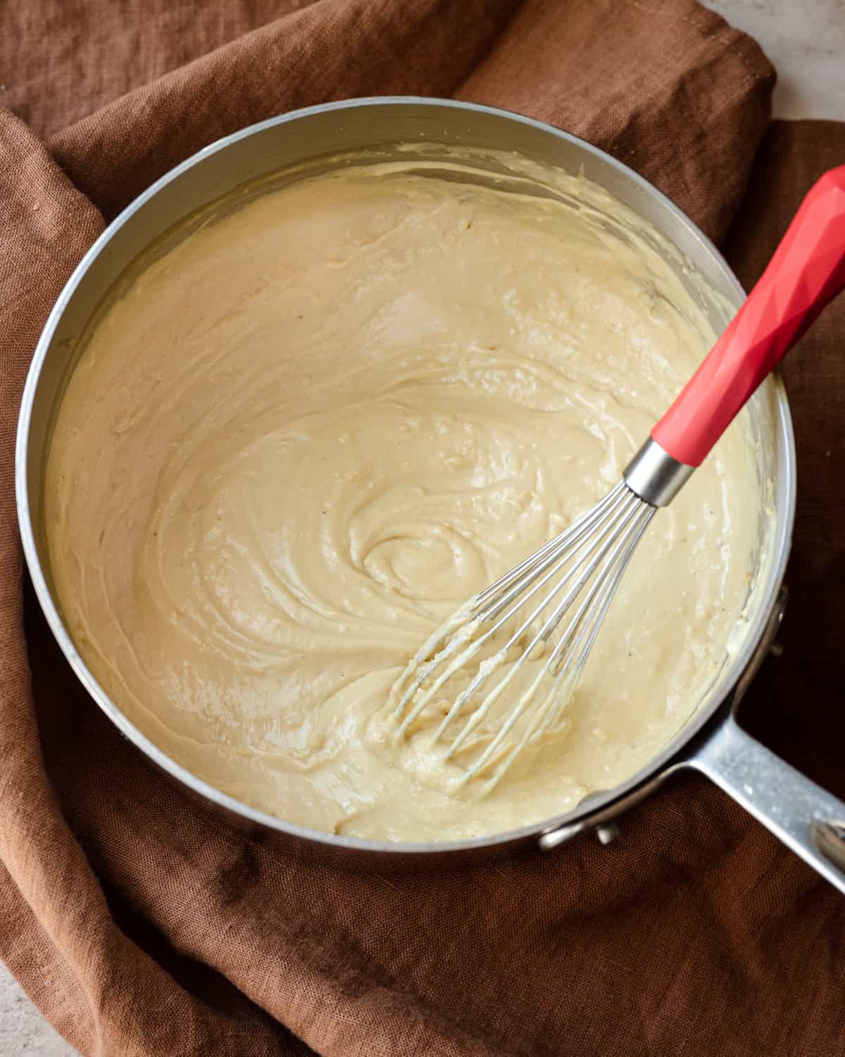a saucepan of a thick vegan bechamel sauce with a whisk in the pan.