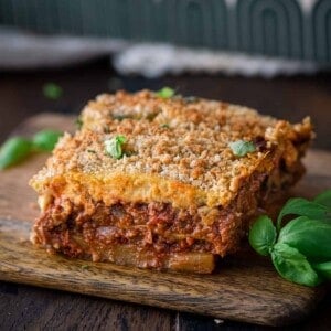 slice of vegan moussaka on a small wooden cutting board with fresh basil on the side.