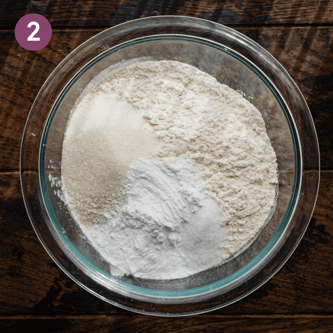 mixture of flour, sugar, baking powder, and salt in a glass bowl on wooden table.