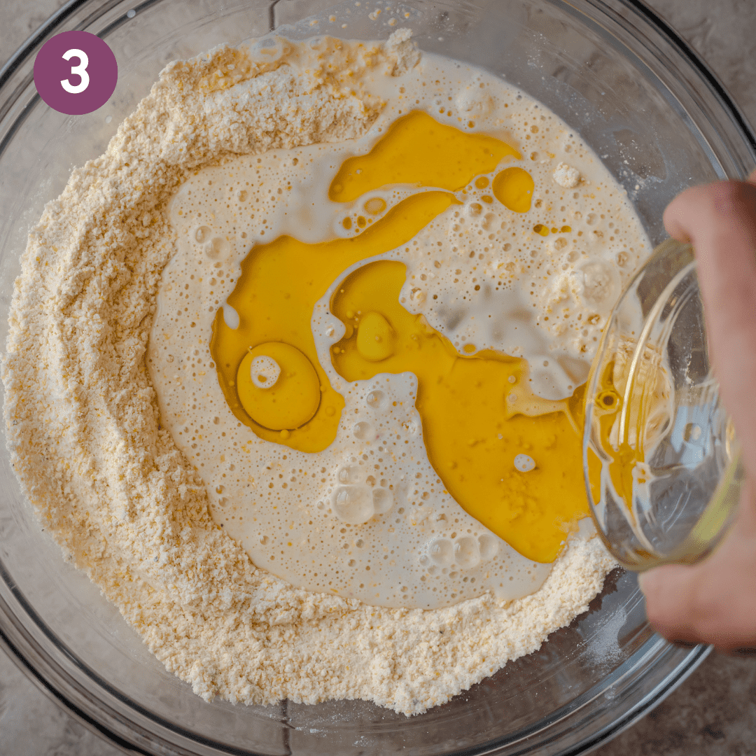 woman's hands pouring melted vegan butter and oil into a cornmeal batter in a glass bowl.