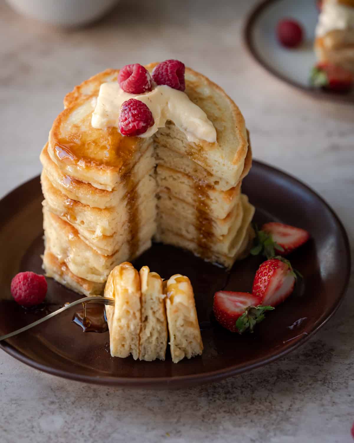 a stack of vegan pancakes sliced into showing the fluffy exterior of the pancakes on a brown plate with berries.