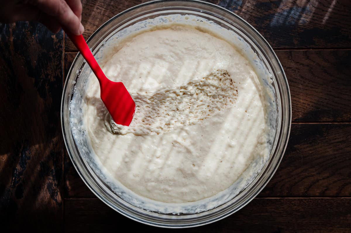 spatula running through a thick, airy vegan pancake batter in a glass bowl.