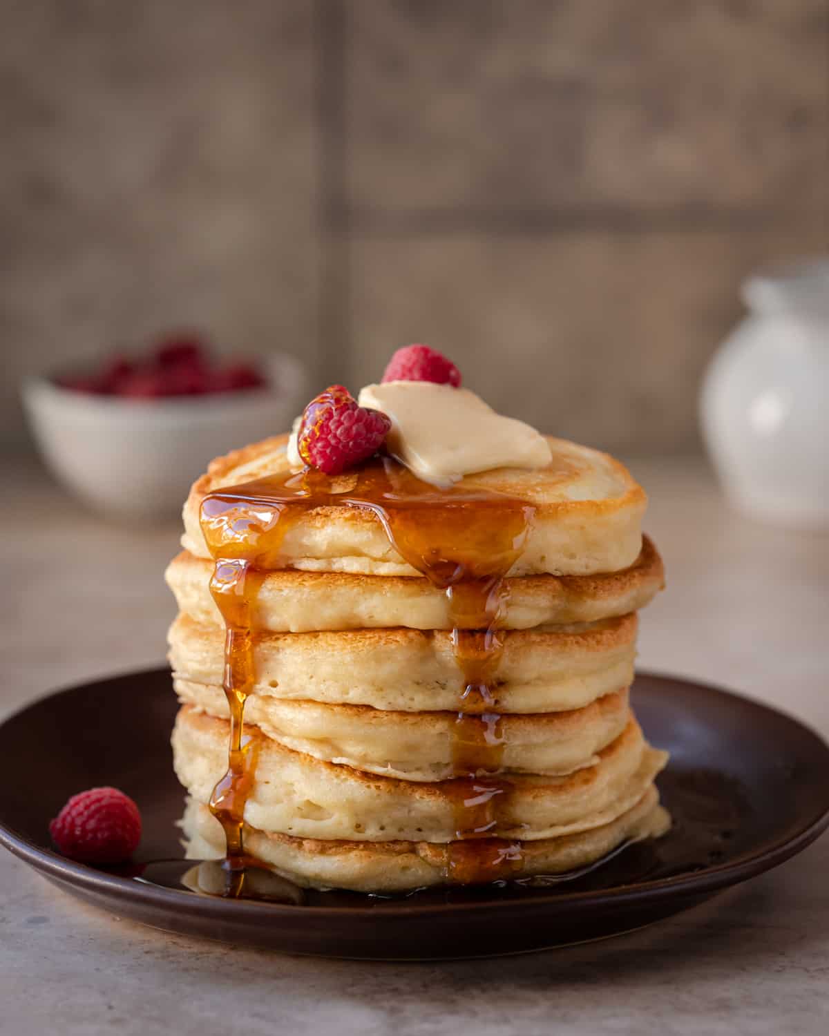 stack of fluffy vegan pancakes on a brown plate with maple syrup drizzling down and butter on top.