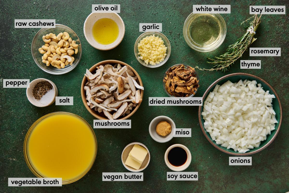 ingredients for vegan mushroom soup in bowls laid out on a green table with ingredients labeled.