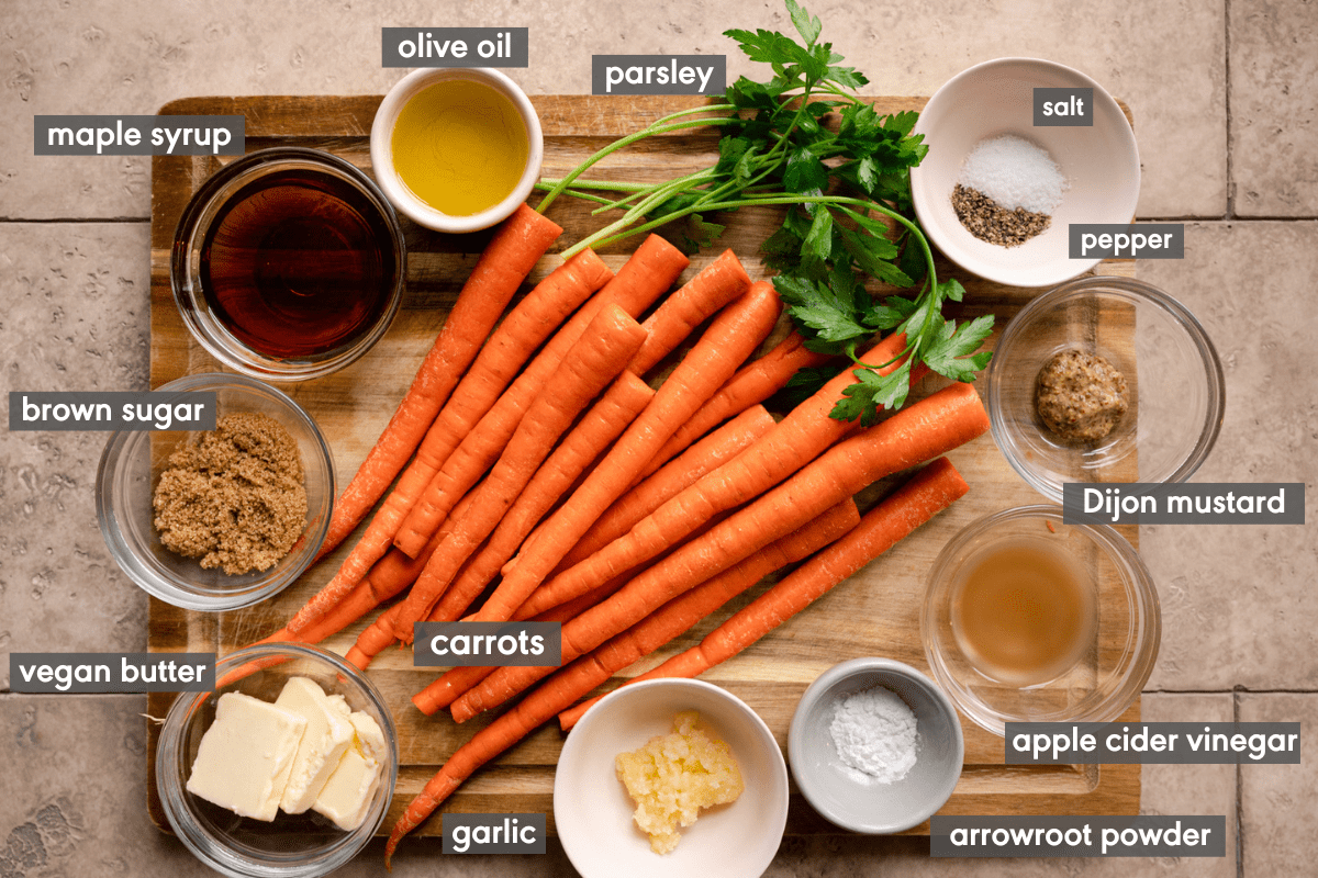 ingredients for maple roasted carrots laid out on a wooden cutting board with names labeled. 