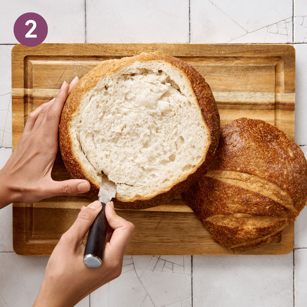 Woman cutting and hollowing out bread bowl.