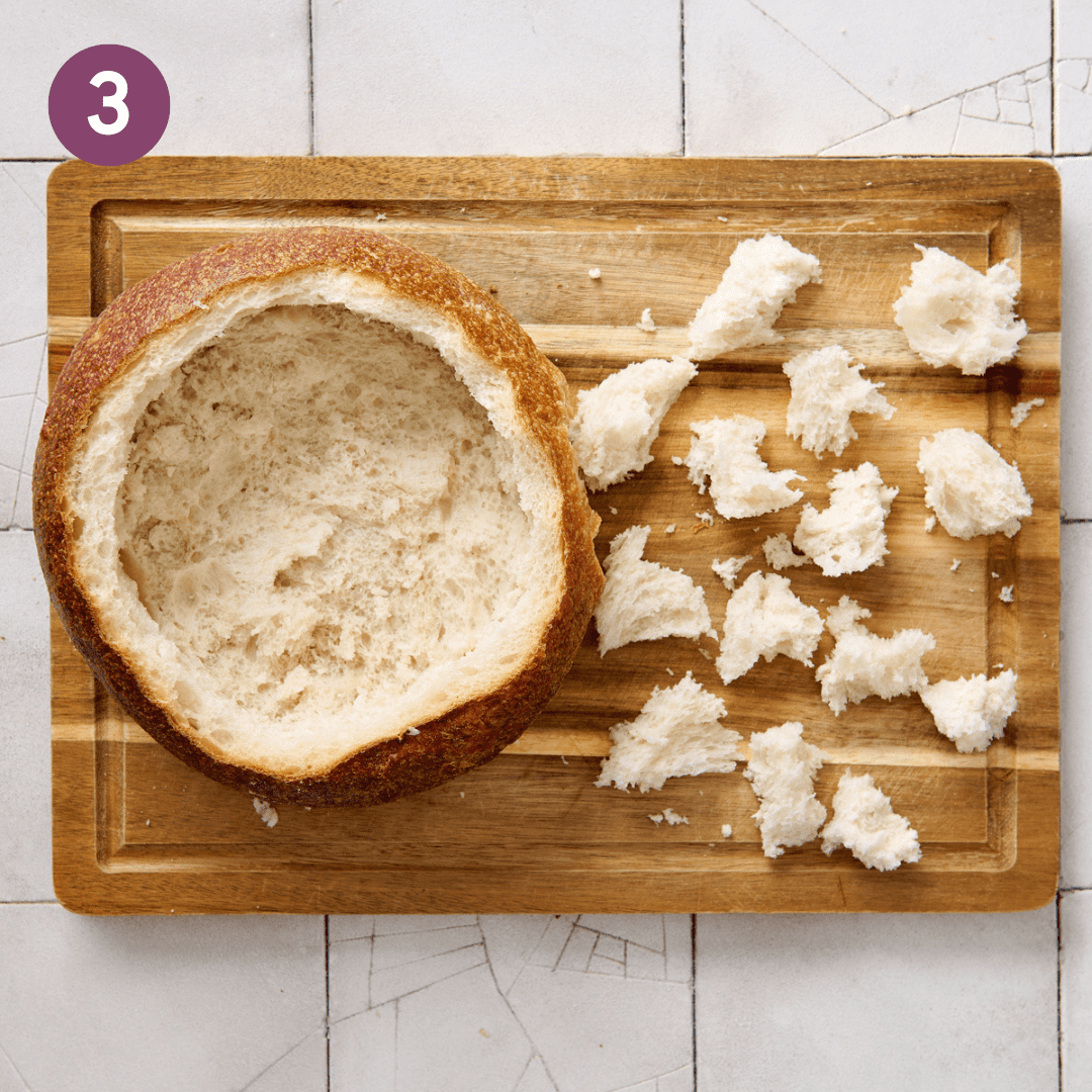 Hollow bread bowl with bite-sized pieces of bread next to it.