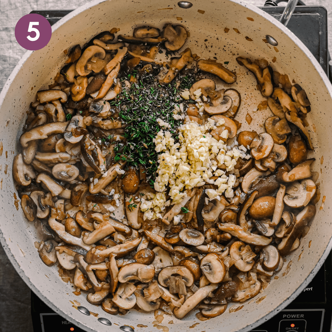 golden brown sauteed mushrooms with garlic and fresh herbs on top in a ceramic saute pan.