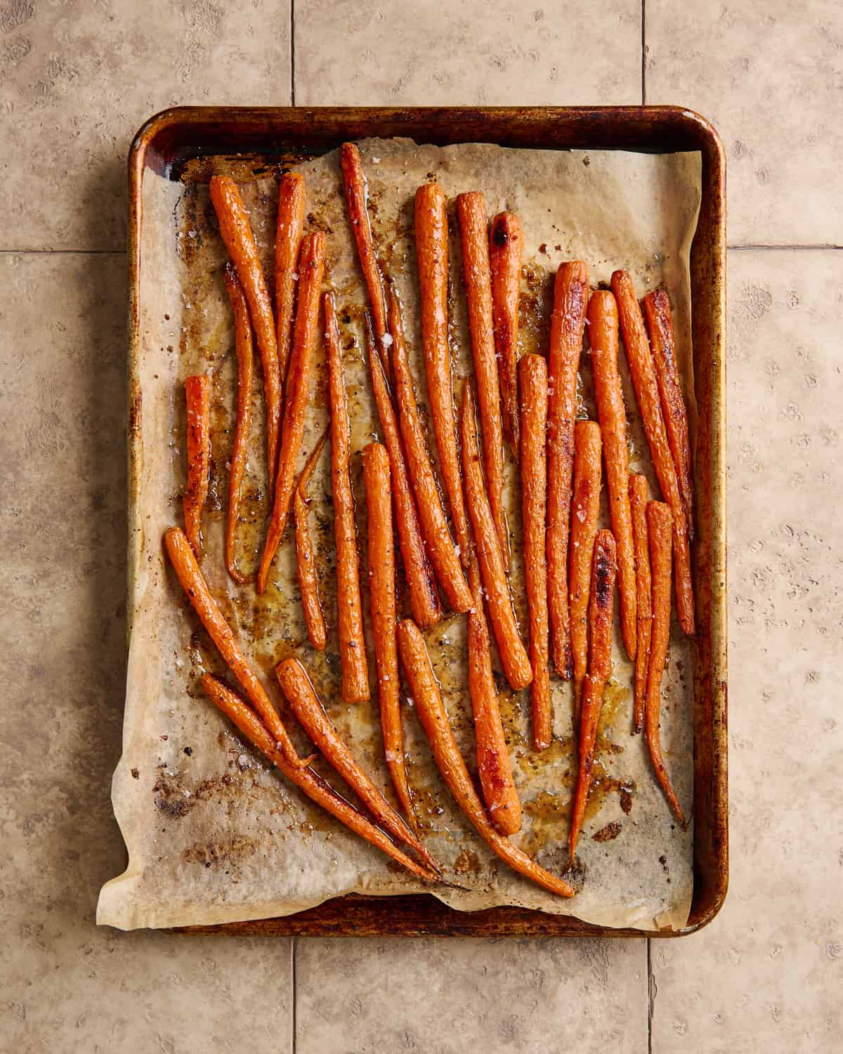 maple glazed carrots on a parchment paper lined sheet pan on a beige tiled surface.