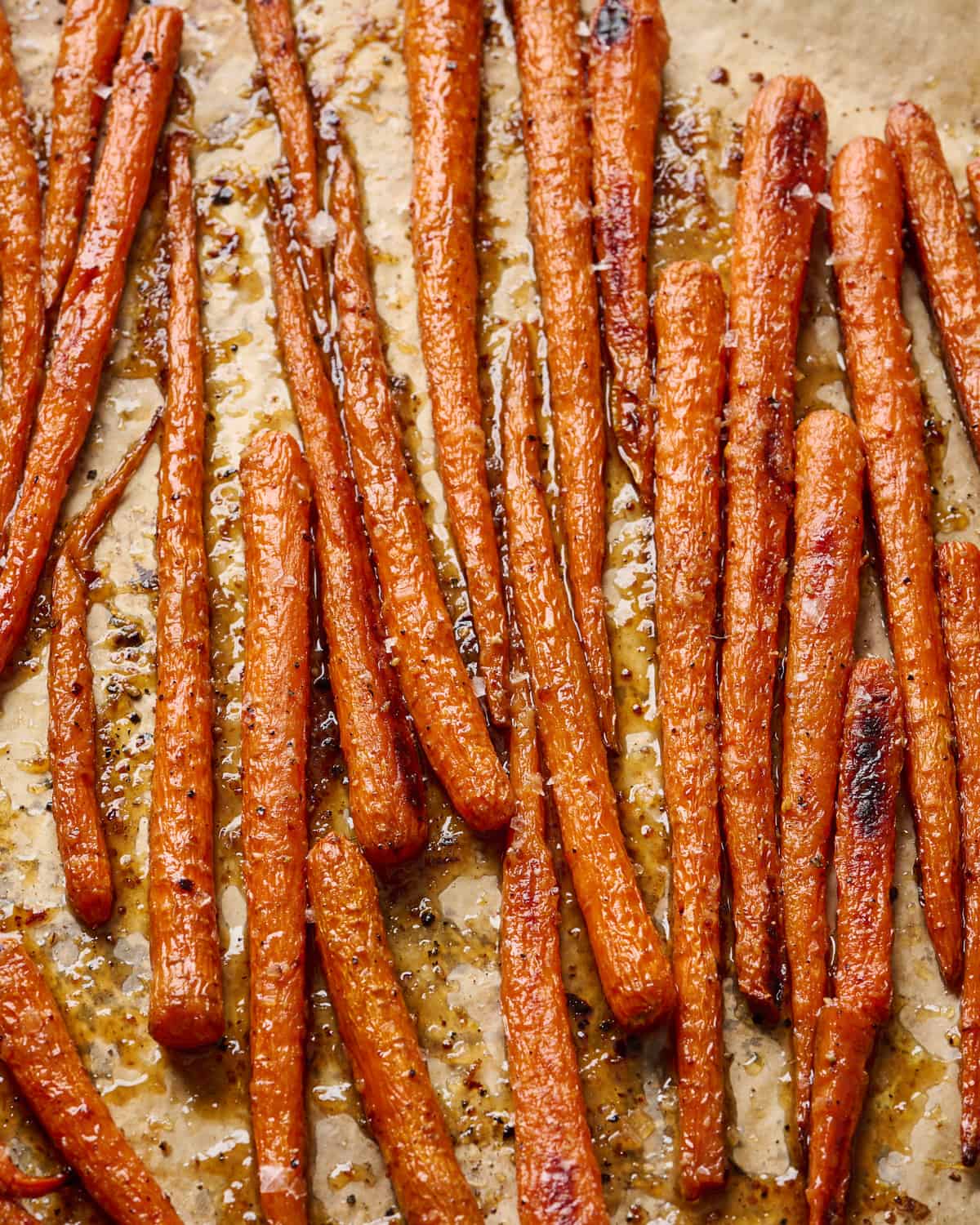 close up angle on maple glazed carrots on a parchment paper lined sheet pan.