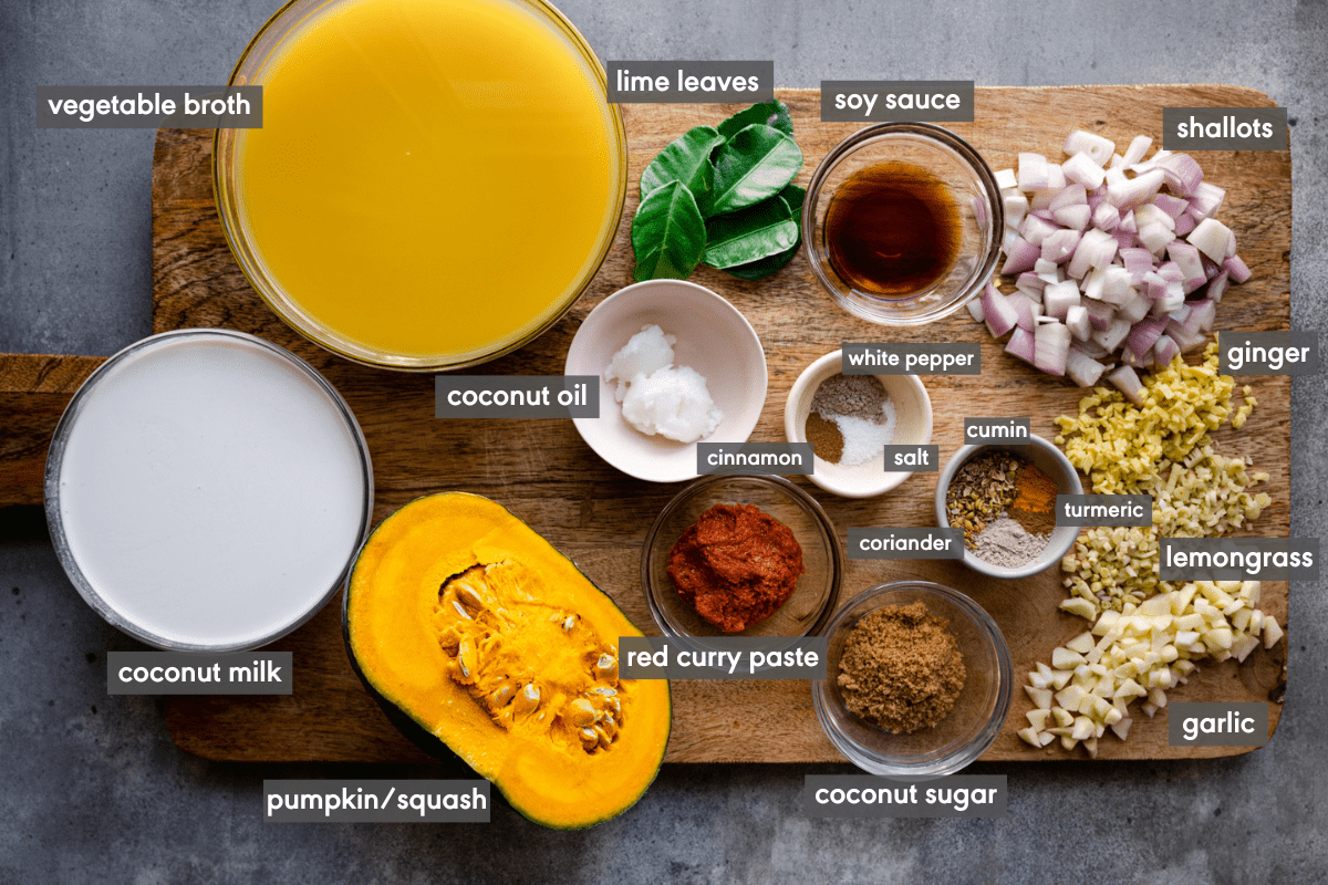 ingredients for a thai pumpkin soup laid out on a wooden cutting board and labeled. 