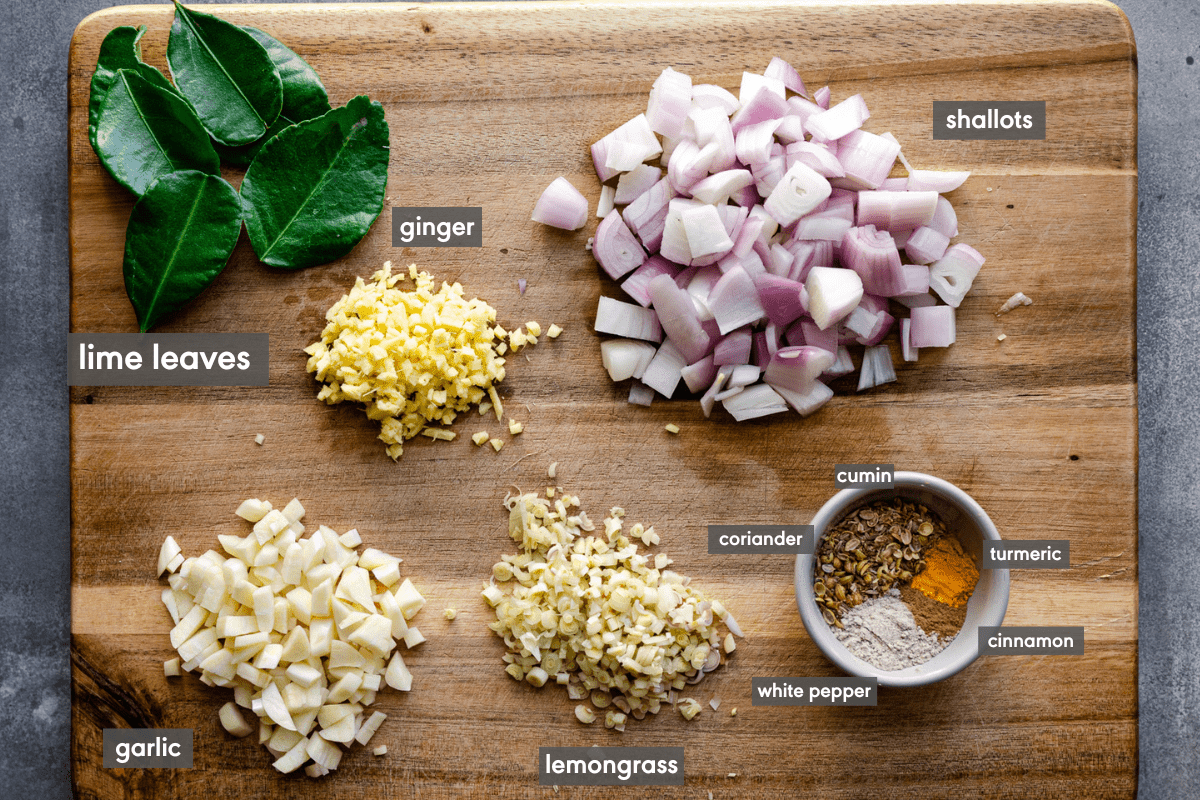 Thai aromatics of garlic, lemongrass, ginger, spices, and lime leaves on a wooden cutting board and labeled. 