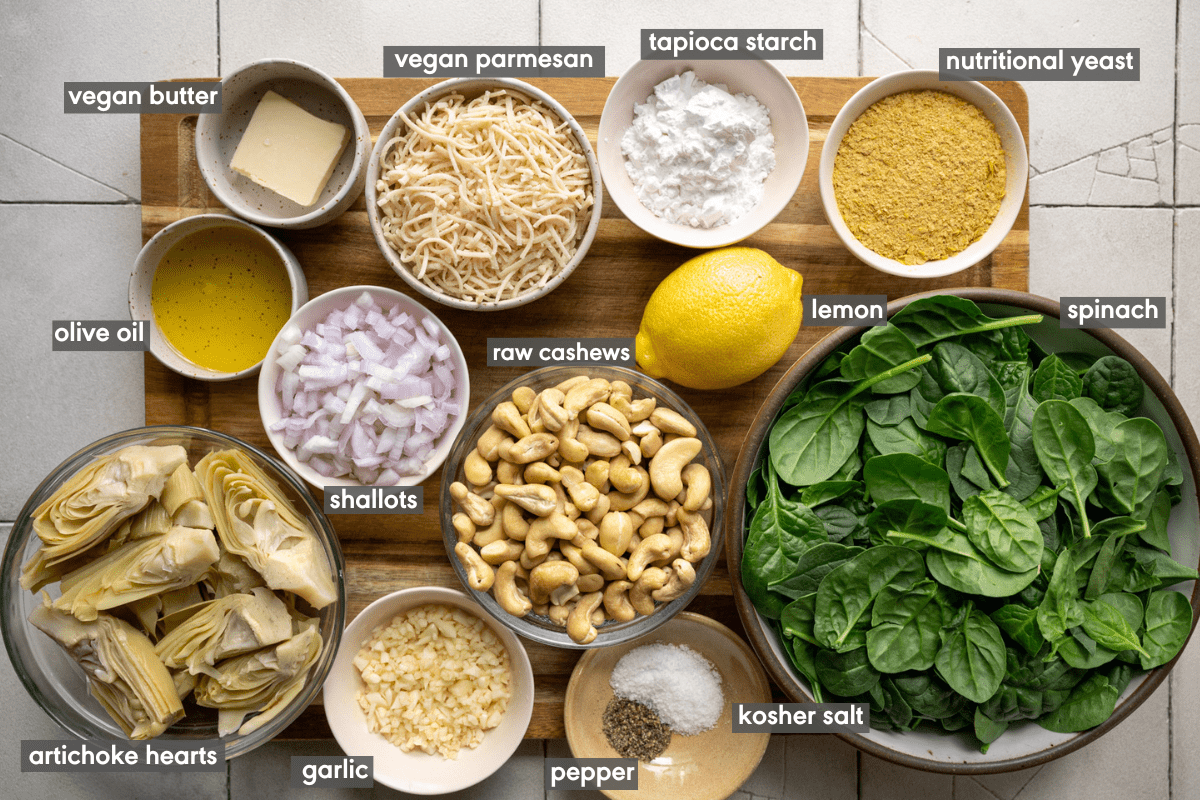 Vegan Spinach Artichoke Dip ingredients in various bowls on a wooden cutting board on a white table.
