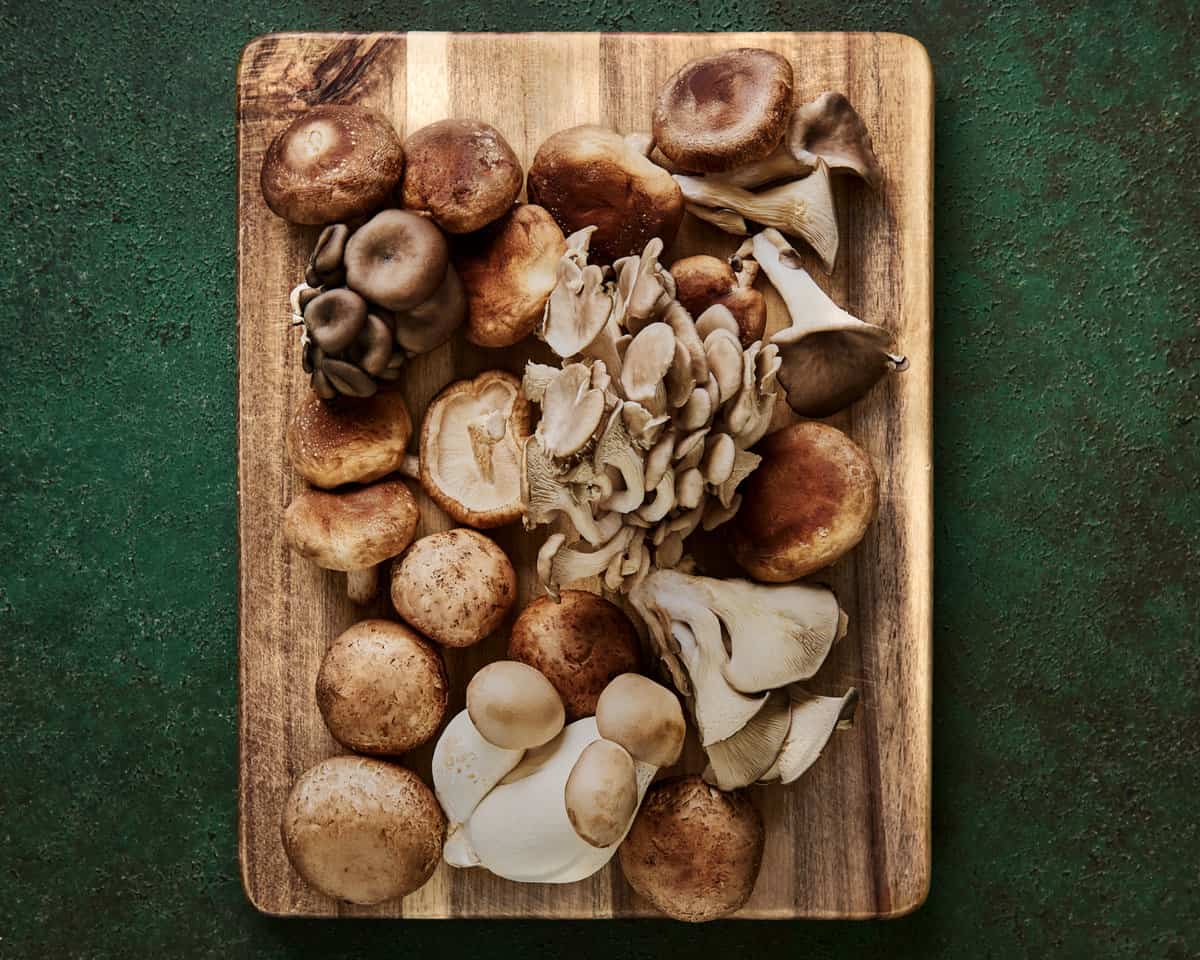a variety of beautiful whole mushrooms on a wooden cutting board on a green surface. 