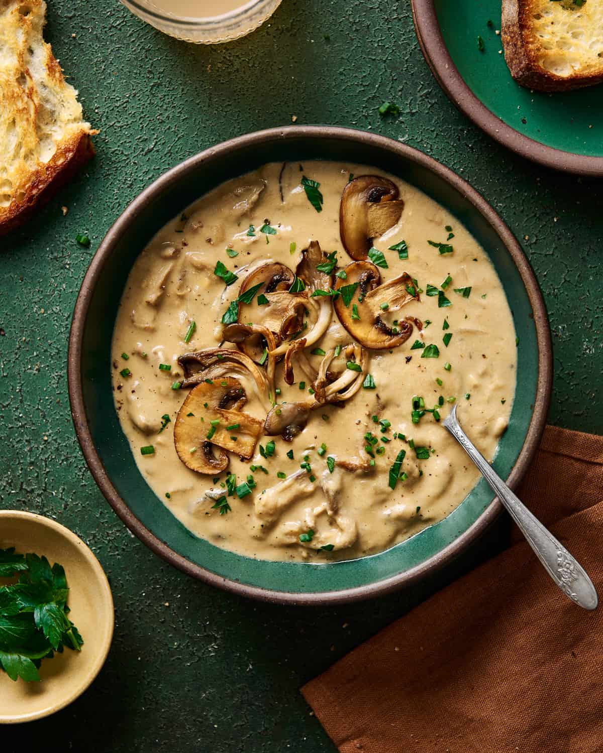 Creamy vegan mushroom soup with seared mushrooms in a green ceramic bowl on a green table.