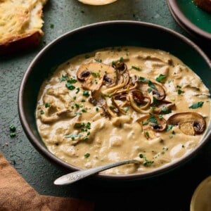 angled backlit shot of creamy vegan mushroom soup in a green bowl with bread and wine in the background.