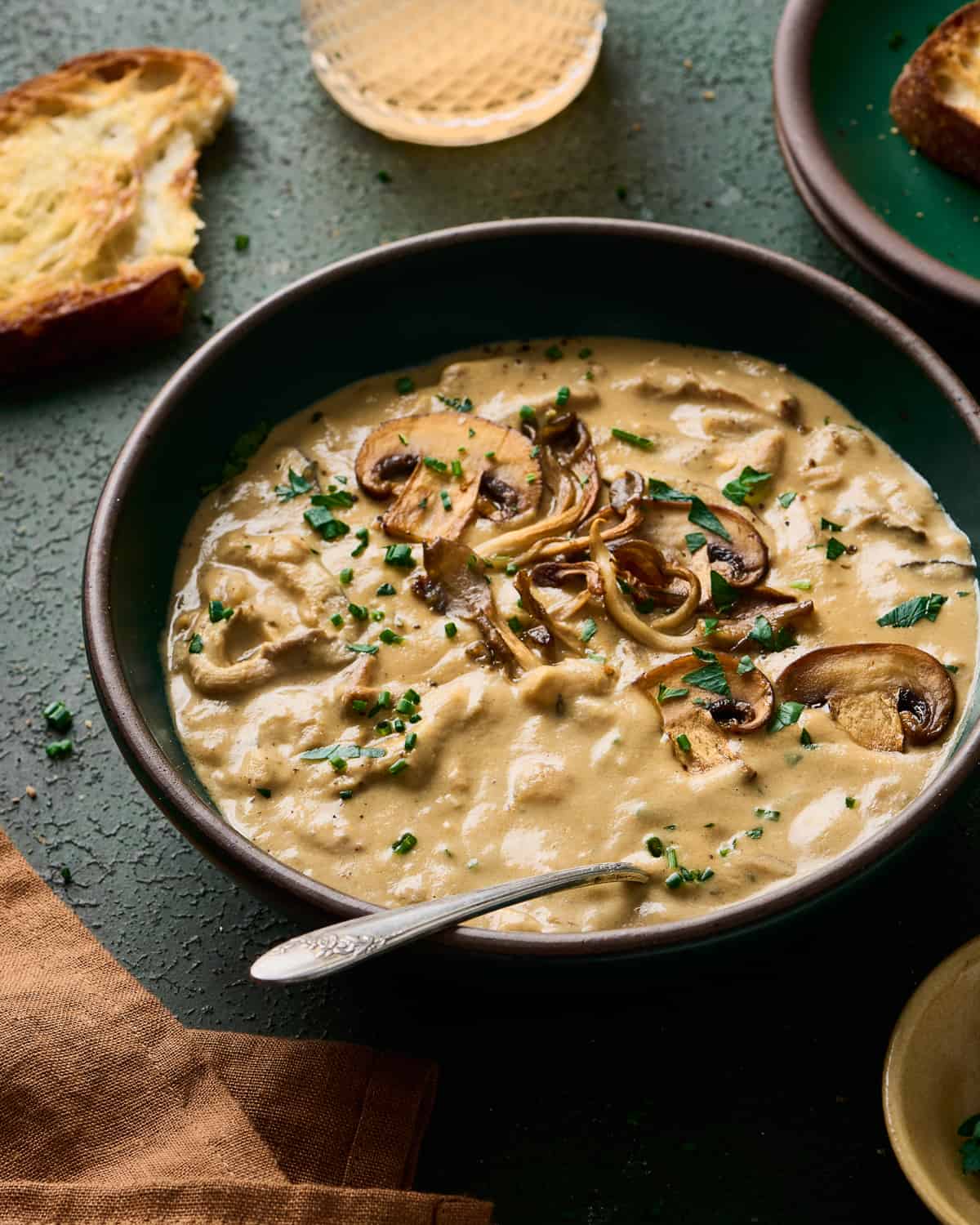 angled backlit shot of creamy vegan mushroom soup in a green bowl with bread and wine in the background. 