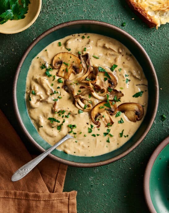 creamy vegan mushroom soup with seared mushrooms on top in a green ceramic bowl on a green table.