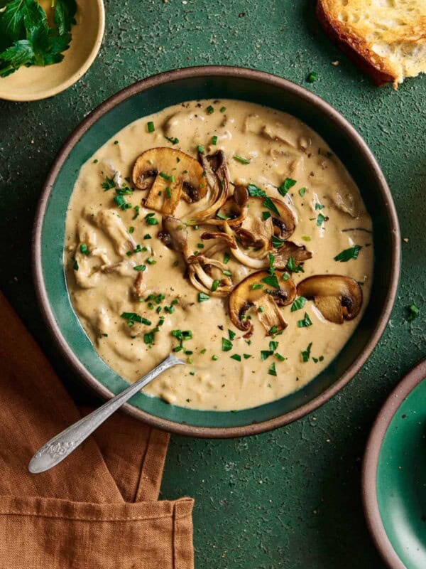 creamy vegan mushroom soup with seared mushrooms on top in a green ceramic bowl on a green table.